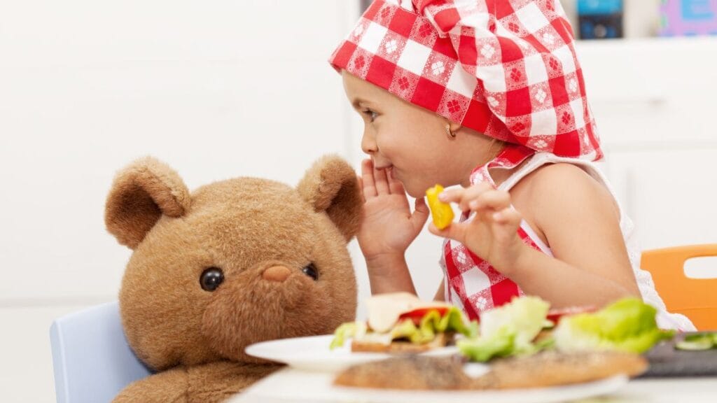 A close-up shot of a colorful and fun kid's meal, featuring a sandwich cut into a star shape, a side of cherry tomatoes, and cucumber slices arranged to look like a caterpillar. The plate is white and the food is arranged to be visually appealing to children, promoting healthy eating habits.